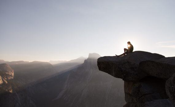 man sitting on cliff during sunrise
